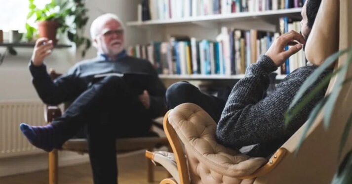 Therapist and client talking in a comfortable counselling room with bookshelves in the background.